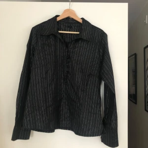 Svart skjorta med glitter - Snygg svart skjorta med glittriga ränder, perfekt för både vardag och fest. Skjortan har långa ärmar. Aldrig använd! 