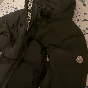 Svart pufferjacka från Moncler - Säljer en svart pufferjacka från Moncler i mycket bra skick. Jackan har en stilren design med Moncler-logga på ärmen och dragkedja framtill. Perfekt för kalla vinterdagar med sin varma och bekväma passform. Passar både till vardags och festliga tillfällen. 🖤
