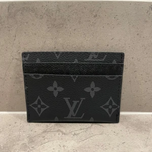 Svart kortfodral från Louis Vuitton - Säljer ett stilrent svart kortfodral från Louis Vuitton med det klassiska monogrammönstret. Perfekt för att hålla dina kort organiserade och snygga. Kortfodralet är i mycket bra skick och passar perfekt för både vardag och fest. En tidlös accessoar för den modeintresserade!