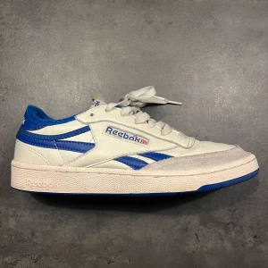 Vita och blå Reebok sneakers club c vintage - Säljer ett par klassiska Reebok sneakers i vitt och blått. Skorna har en snygg retrostil med snörning och Reebok-loggan på sidan. De är i bra skick med lite crease ovanpå. Nypris 1350kr på Zalando.