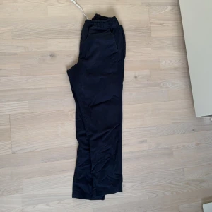 Marinblå chinos från Polo Ralph Lauren - Säljer ett par svarta byxor från Polo Ralph Lauren i stretchigt material. De har en elastisk midja med snörning och knapp för extra komfort. Perfekta för en avslappnad stil men ändå snygga nog för vardagsbruk. Passar bra till både höst och vår.