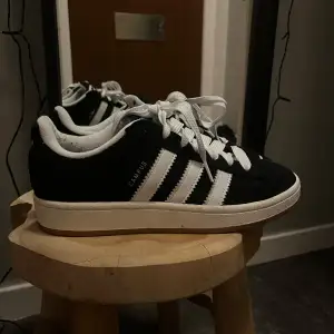 Säljer ett par snygga svarta Adidas Campus sneakers i mycket bra skick. De har de klassiska vita ränderna och en bekväm passform. Perfekta för både vardag och fest! 🖤