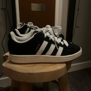 Svarta Adidas Campus sneakers - Säljer ett par snygga svarta Adidas Campus sneakers i mycket bra skick. De har de klassiska vita ränderna och en bekväm passform. Perfekta för både vardag och fest! 🖤