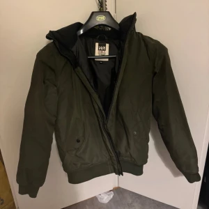 Olivgrön bomberjacka från W.A. - Säljer en olivgrön bomberjacka från W.A. i bra skick. Jackan har en dragkedja framtill och ribbade muddar vid ärmslut och nederkant. Perfekt för höst och vår, med en stilren och klassisk look. Passar både till vardags och lite mer uppklädda tillfällen.