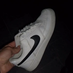 Nike Air Force i vitt och svart - Säljer ett par klassiska Nike Air Force sneakers i vitt med svart swoosh. Skorna har snörning och är i bra skick, perfekta för både vardag och fest. De är bekväma och stilrena, en riktig garderobsklassiker!