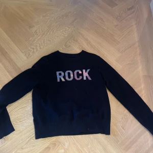 Svart tröja med 'ROCK' från Zadig & Voltaire - Säljer en cool svart tröja från Zadig & Voltaire med texten 'ROCK' i silver på framsidan. Tröjan har långa ärmar och är perfekt för en avslappnad stil. Passar bra till både jeans och kjol. Perfekt för höst och vinter!