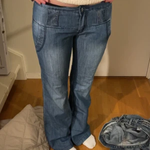 lowwaisted bootcut med fina detaljer - Säljer ett par snygga blå jeansbyxor med bootcut. De har en låg midja och dekorativa sömmar vid fickorna. Perfekta för en avslappnad stil och passar till både vardag och fest. Sköna och trendiga!