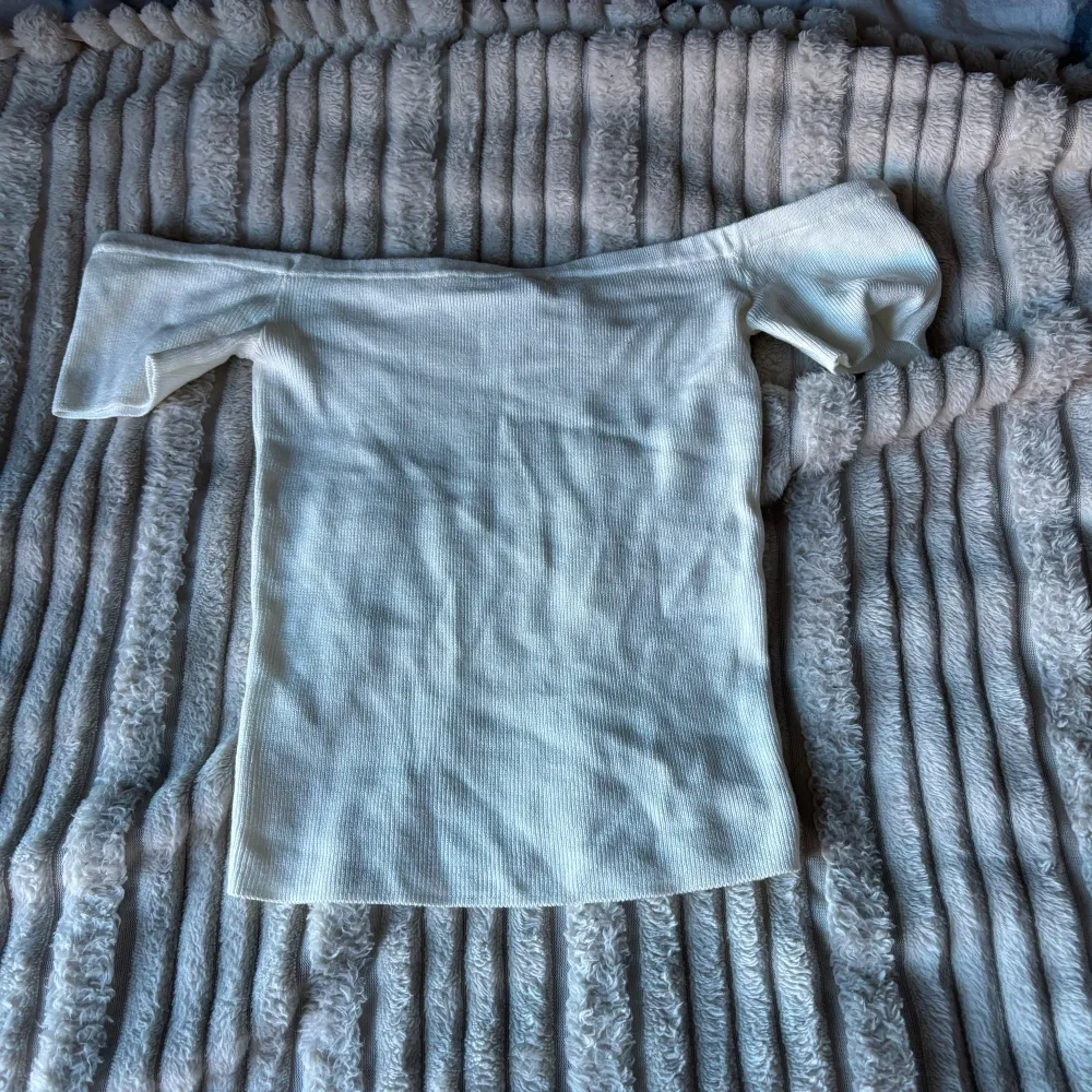 Säljer en superfin vit ribbad offshoulder topp från H&M Divided i storlek XS. Perfekt för sommardagar eller en utekväll. Toppen har en tight passform och är i mycket bra skick. Passar både till jeans och kjol för en stilren look.. Toppar.