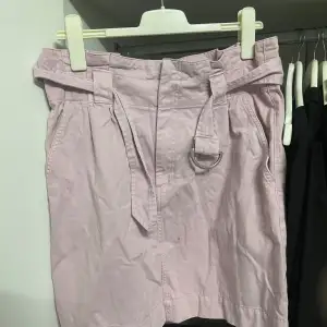 Säljer en superfin ljuslila kjol från H&M i storlek L. Kjolen har ett bälte med metallring som ger en snygg detalj och perfekt passform. Den är gjord i ett bekvämt bomullsmaterial, perfekt för vår och sommar. Passar både till vardags och fest! 🌸