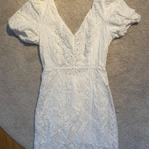 Vit spetsklänning med puffärmar - Säljer en superfin vit klänning i spets med puffiga kortärmar och v-ringning. Perfekt för sommarens fester eller studentfirande! Klänningen har en tight passform och är i mycket bra skick med öppen rygg! Bärde själv på min egna student!