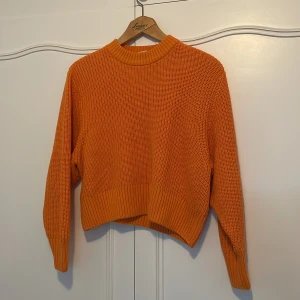 Orange stickad tröja från Monki - Säljer en superfin orange stickad tröja från Monki i storlek S. Den har en croppad passform och långa ärmar, perfekt för höst och vår. Tröjan är i mycket bra skick och har en härlig ribbad struktur vid ärmslut och nederkant. Perfekt för att liva upp garderoben! 🍂