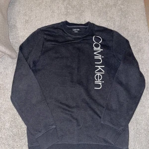 Calvin Klein tröja - Säljer en stilren svart tröja från Calvin Klein i storlek XS. Tröjan har en klassisk design med långärmade ärmar och Calvin Klein-loggan tryckt vertikalt på framsidan. Skriv vid minsta lilla fundering✍️😀✅