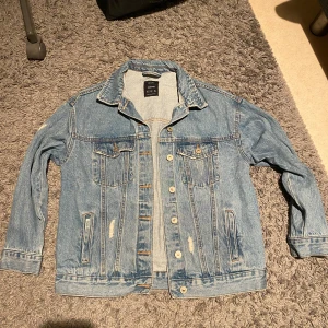 Blå jeansjacka från Bershka - Säljer en klassisk blå jeansjacka från Bershka i storlek M. Jackan har en normal passform med långa ärmar och knappar framtill. Perfekt för vår och höst! Den har en sliten look med snygga detaljer och är i bra skick.