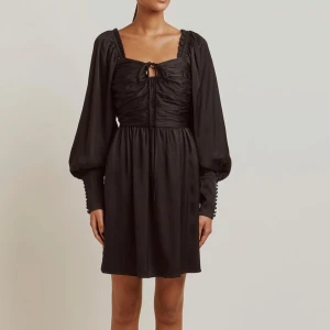 Svart klänning från By Malina - Säljer min helt oanvända By Malina klänning! Snygg svart klänning med långa puffärmar och en elegant knytning framtill. Den har en smickrande passform med dragkedja bak och är perfekt för höst- och vinterfester. Materialet känns lyxigt och ger en fin siluett.