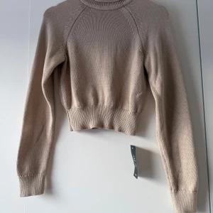 Beige stickad tröja från NA-KD - Säljer en superfin beige stickad tröja från NA-KD. Den är helt ny med tag kvar! Tröjan har en croppad passform och långa ärmar, perfekt för höst och vår. Den ribbade kanten ger en snygg detalj och den är både stilren och bekväm. Perfekt att matcha med jeans eller kjol för en avslappnad look.