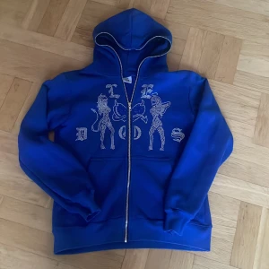 Rhinestone tröja zip Hoodie  - Säljer en riktigt schysst blå rhinestone zip hoodie i storleken S.|Tröjan har ett unikt tryck på framsidan och är från Le Dos.|Perfekt för höst och vår, med långa ärmar och en bekväm passform.| Sparsamt använd utan tecken på hål, skick 9/10.