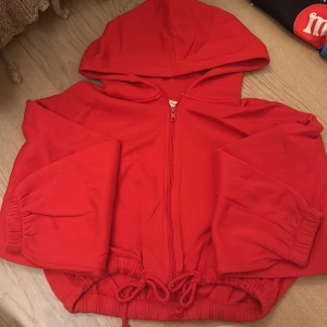 Röd hoodie med dragkedja - Säljer en supermysig röd hoodie med dragkedja och huva. Den har långa ärmar och en praktisk dragsko i nederkanten för justerbar passform. Perfekt för kyliga dagar eller som ett extra lager. Passar både till vardags och chillkvällar. 🧡 liten fläck på armen på sista bilden 💗