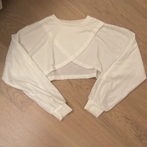 Vit croppad tröja med omlott-design - Säljer en superfin vit croppad tröja med en unik omlott-design framtill. Tröjan har långa ärmar med ribbade muddar som ger en skön passform. Perfekt för både vår och sommar! 🌼