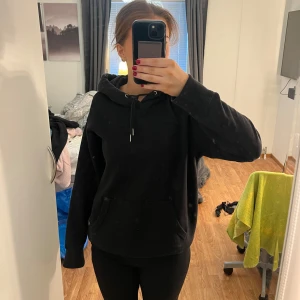 Svart hoodie - Mysig svart hoodie i bra skick. Perfekt för höst och vinter med sin varma och bekväma passform. Har en klassisk känguruficka och justerbar huva med snören. Passar perfekt för en avslappnad stil eller mysiga hemmakvällar.