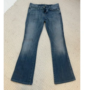 Blå bootcut jeans med unika bakfickor - Säljer ett par snygga blå bootcut jeans i bra skick. De har coola rosa broderade detaljer på bakfickorna som ger en unik touch. Midjemåttet: ca 78cm. Innerbenslängden: ca 78cm