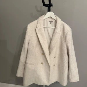 Vit kavaj från H&M - Säljer en stilren vit kavaj från H&M i storlek XL. Den har en dubbelknäppt design med snygga knappar och är gjord i ett texturerat material som ger en lyxig känsla. Perfekt för både vardag och fest! Skulle beskrivs färgen som vit/creme färgad. 