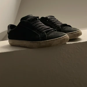  Svarta Arigato  sneakers i mocka - Säljer ett par svarta sneakers i mocka med snörning. De har en vit sula som är lite smutsig, men skorna är i bra skick. Perfekta för vardagsbruk och passar till det mesta i garderoben. Sköna och stilrena!