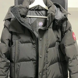 Svart dunjacka från Canada Goose - Säljer en svart dunjacka från Canada Goose i storlek M. Jackan är i mycket bra skick och perfekt för vintern. Den har en dragkedja och knappar framtill, samt en praktisk huva. Supervarm och stilren för kalla dagar! ❄️