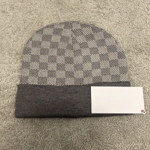 L.v mössa - Säljer en snygg grå rutig mössa i mycket bra skick. Den är perfekt för höst och vinter, med ett stilrent mönster och ribbad kant. Mössan är mjuk och bekväm, idealisk för att hålla värmen under kyliga dagar.