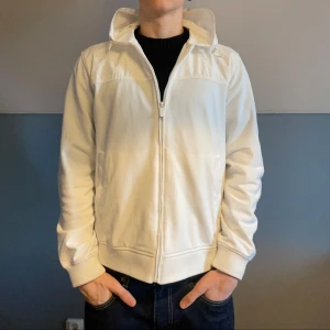 Massimo Dutti Cardigan  - Säljer en stilren vita limited edition cardigan från Massimo Dutti i storlek M. Den har en dragkedja framtill och en bekväm huva. Perfekt för både vår och höst, med långa ärmar och en skön passform. Passar till alla tillfällen.