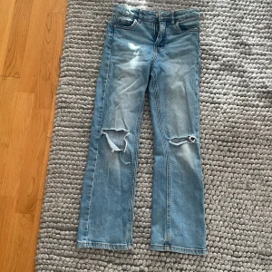 Blå jeans med slitningar - Säljer ett par blå jeans i bra skick men ett hål har blivit lite större en det andra eftersom jag råkade ta ner foten där när jag skulle sätta på mig dom 😅. De har en straight passform och är perfekta för en avslappnad stil. Jeansen är midwaist och gjorda av klassiskt denimtyg. Perfekta för både vardag och fest!