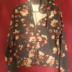 Blommig hoodie med dragkedja - Säljer en superfin hoodie med blommigt mönster. Den har en dragkedja framtill och en mysig huva. Perfekt för höst och vår när du vill vara både bekväm och stilren. 