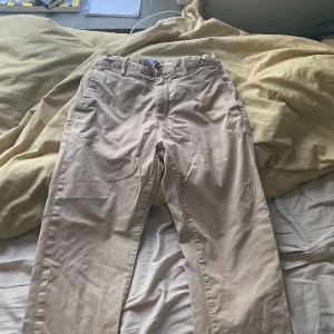 Beige chinos(Gant) - Säljer ett par klassiska beige chinos i bra skick. De har en normal passform och är perfekta för både vardag och lite mer uppklädda tillfällen. Byxorna har knappar och dragkedja framtill samt fickor både fram och bak. Perfekta för vår och höst!