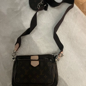 Brun axelväska med monogram - Säljer nu min bruna axelväska med monogrammönster och axelrem. Väskan har flera fack med dragkedja och detaljer i ljusare färg.
