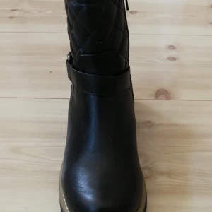 Svarta boots från Duffy - Helt nya, oanvända barnskor i storlek 36. Snygga svarta boots från Duffy i skinn med quiltad detalj upptill. De har en praktisk dragkedja på sidan och ett bälte runt ankeln för extra stil. Perfekta för höst och vinter med en robust sula som ger bra grepp. Dessa boots är både bekväma och trendiga, idealiska för vardagsbruk.