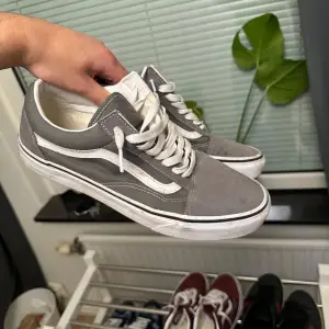 Säljer ett par gråa Vans sneakers i bra skick. De har en klassisk design med vit sula och vita snören.