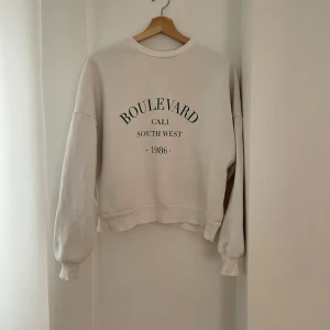 Vit sweatshirt från Only Trend - Säljer en vit sweatshirt från Only Trend i storlek XS. Den har trycket 'Boulevard Cali South West 1986' på framsidan. Tröjan är i bra skick och perfekt för en avslappnad stil. Den har långa ärmar och en ribbad krage.