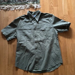 Grön kortärmad skjorta från Levi's All-Duty - Säljer en snygg grön kortärmad skjorta från Levi's i storlek L. Skjortan är i bra skick och har en klassisk krage med knappar framtill.