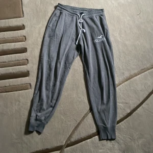 Grå mjukisbyxor från Hollister - Säljer ett par grå mjukisbyxor från Hollister i storlek M. De är superbekväma med en elastisk midja, fickor på var sin sida. Byxorna har en broderad Hollister-logga på sidan och är perfekta för en avslappnad dag hemma eller på språng.
