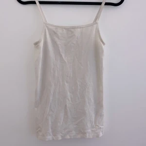Vit linnetopp - Säljer en enkel och stilren vit linnetopp med smala axelband. Perfekt för varma sommardagar eller som ett basplagg under en tröja. Toppen är i ett mjukt och bekvämt material.