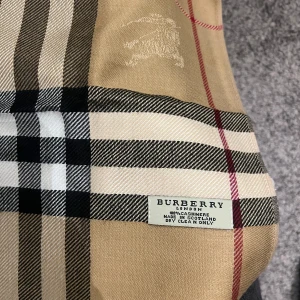 Rutig halsduk från Burberry - Säljer en klassisk rutig halsduk från Burberry i beige, svart och rött. Den är gjord av mjuk kashmir och har fransar i kanterna. Perfekt för att hålla sig varm och stilren under kyliga dagar. Passar både höst och vinter. 🧣✨