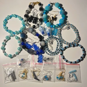 20 Färgglada smycken i olika stilar - Ett set med färgglada smycken, inklusive armband och örhängen. Armbanden är i olika nyanser av blått, svart och silver, med pärlor och glittriga detaljer. Örhängena finns i olika stilar, med både pärlor och metalliska detaljer. Perfekt för att liva upp vilken outfit som helst!