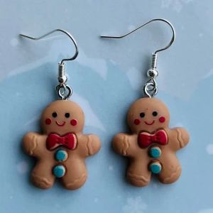 Pepparkaksörhängen med röd rosett - Supergulliga örhängen formade som pepparkaksgubbar med röda rosetter och blå knappar. Perfekta för att sprida julstämning! De är lätta och bekväma att bära hela dagen. Passar perfekt till julens alla fester och tillfällen. Nickelfria krokar. Hämtas i Hornstull i Stockholm eller skickas mot fraktkostnad. ✨
