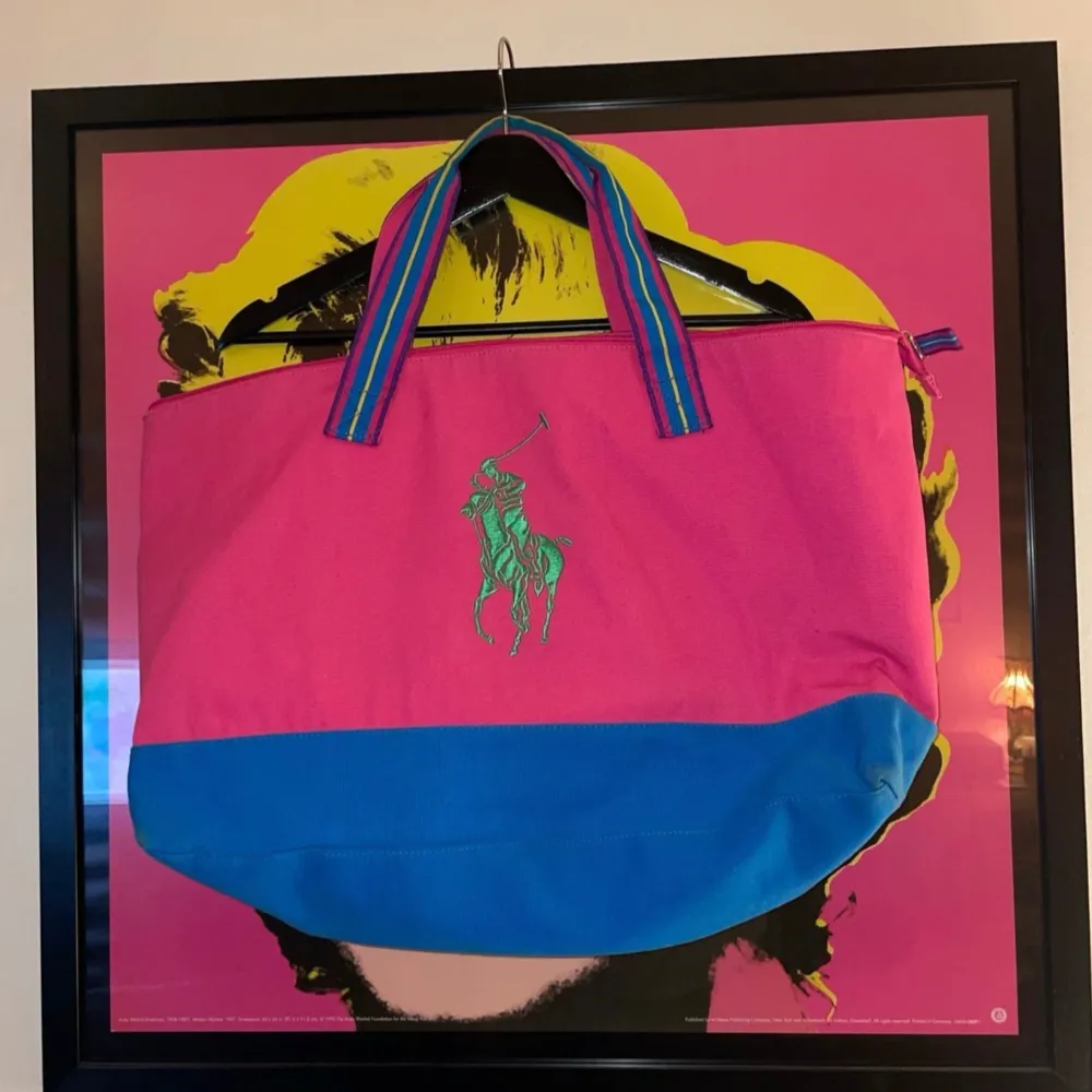 Säljer en supercool och färgglad väska från Ralph Lauren. Den är rosa med en blå botten och har ett stort grönt logotryck på framsidan. Handtagen är randiga i flera färger vilket ger en extra pop av stil. Perfekt för sommarens alla äventyr! 👜🌈. Väskor.