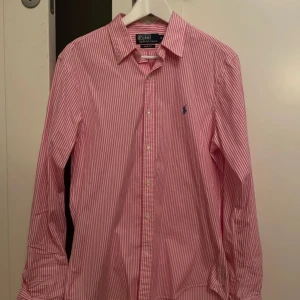 Rosa och vit randig skjorta från Polo Ralph Lauren - Säljer en snygg rosa och vit randig skjorta från Polo Ralph Lauren i storlek M. Perfekt för både vardag och fest! 💖