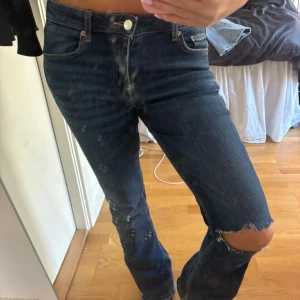Mörkblå jeans med slitningar - Säljer ett par mörkblå jeans med coola slitningar vid knäna. De har en klassisk femficksdesign och en knappgylf. Perfekta för en avslappnad vardagslook eller en utekväll. Passar bra med sneakers eller boots!