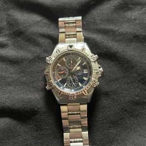 Silverfärgad klocka från Seiko - Säljer en snygg och robust Seiko-klocka från 1992 i silverfärgat stål. Den har en mörk urtavla med flera små urtavlor och datumvisning. Armbandet är i rostfritt stål och har en säker låsning. Perfekt för både vardag och fest. Original pris ligger runt 4500-5000.