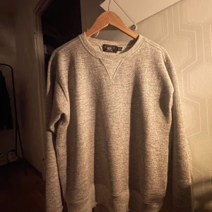 Grå tröja från Ralph Lauren, Splitterny  - Säljer en bekväm grå tröja från RRL  Ralph Lauren. Perfekt för både vardag och avslappnade tillfällen. Tröjan har långa ärmar och en klassisk rund halsringning. Den är i bra skick och passar perfekt till höst- och vintergarderoben. Nypris: 2500kr