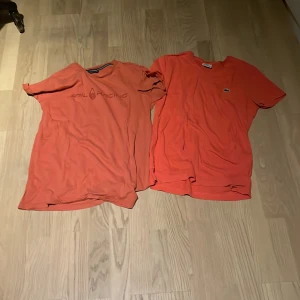 Två röda t-shirts från Sail Racing och Lacoste - Säljer två snygga orange t-shirts. Den ena är från Sail Racing med tryck på bröstet och den andra från Lacoste med den klassiska krokodilloggan. Perfekta för en avslappnad stil. Båda är kortärmade och i bra skick. Passar perfekt till sommaren! 🌞