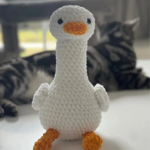 Handgjord vit gås - Säljer en supergullig handgjord virkad gås i vitt garn med orange näbb och fötter. Den är perfekt som dekoration eller som en mysig kompis att krama. Gåsen har en lång hals och små vingar på sidorna. Perfekt present till någon som älskar unika och handgjorda saker! 🦢✨