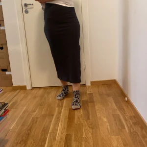 Grå ribbad kjol f - Säljer en snygg grå/svart ribbad kjol från nly trend i storlek S. Kjolen är lång och har en stilren slits på sidan som ger en extra touch. Perfekt för både vardag och fest! 🖤